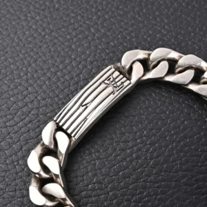 Louis Vuitton Monogram chain bracelet with engraved logo detail, showcasing a silver Cuban chain design on a textured black background.