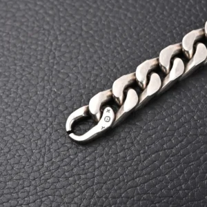 Louis Vuitton Monogram chain bracelet close-up, featuring engraved logo and metal links, set against a textured black background.