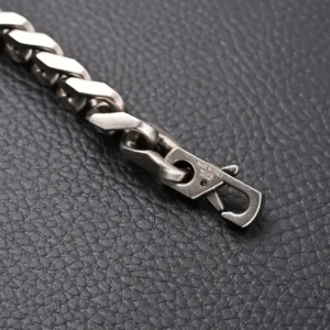 Louis Vuitton Monogram chain bracelet featuring a silver Cuban link design and clasp, displayed on a textured black surface.