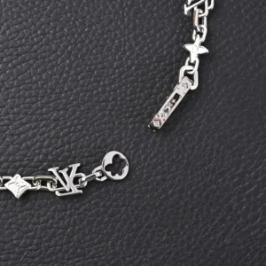 Louis Vuitton LV Monogram Craggy chrysanthemum necklace featuring glossy brass links, LV logo, and floral elements, set against a textured black background.