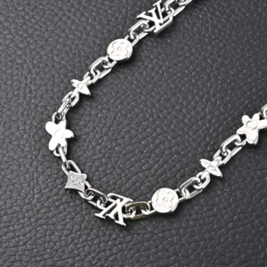 Louis Vuitton LV Monogram Craggy chrysanthemum necklace featuring glossy brass links and iconic logos, displayed on a textured black surface.