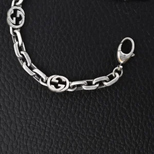 Gucci Letter Double Interlocking Silver Bracelet featuring interlinked G logos on a textured black background, highlighting its design and luxury appeal.