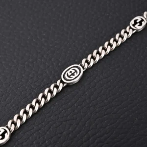 Gucci chain bracelet silver metal black enamel interlocking G logo accents on black leather background