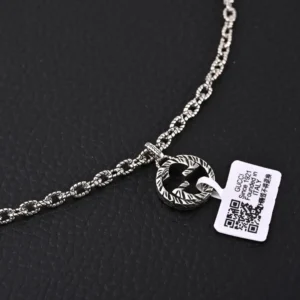 Gucci GUC 3D Double G Pure Silver Pendant Necklace featuring a detailed pendant and chain, displayed on a textured black surface, with a product tag attached.