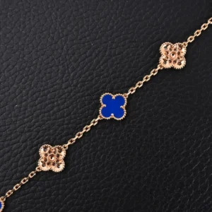 Van Cleef & Arpels replica bracelet featuring blue fritillaria and four-leaf clover motifs, crafted in high-quality 925 silver with 18K gold electroplating, displayed against a textured black background.