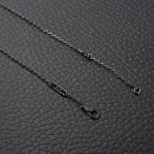 Black chain necklace with clasp details, showcasing the design of the Van Cleef Arpels Flower Necklace, set against a textured dark background.