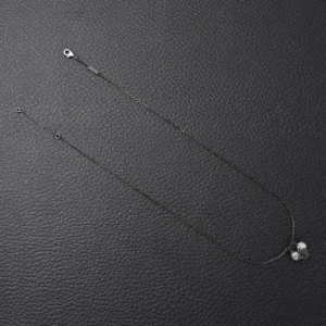 Van Cleef Arpels Flower Necklace on a textured black surface, featuring a delicate chain and floral pendant design, highlighting luxury jewelry aesthetics.