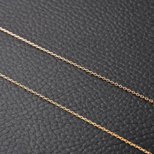 No brand or model information visible; image shows two delicate gold chains on textured black leather background
