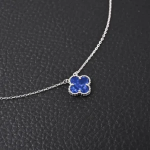 Van Cleef Arpels Classic Clover Necklace featuring a blue clover pendant on a silver chain, set against a textured black background.