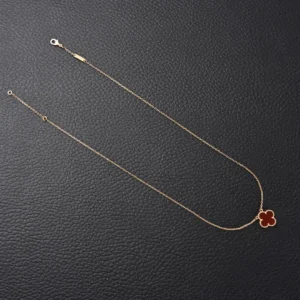 Van Cleef & Arpels Classic Clover Necklace in gold with red enamel pendant, displayed on a dark leather background.