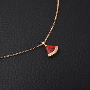 BVLGARI Diva fan-shaped necklace featuring a red agate pendant with white mother of pearl and diamond accents, on a delicate gold chain, against a textured black background.