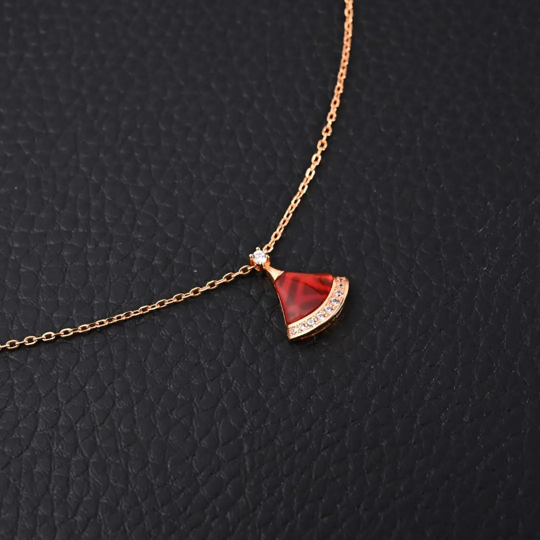BVLGARI Diva fan-shaped necklace featuring red agate, white mother of pearl, and diamonds on a delicate chain, set against a textured black background.