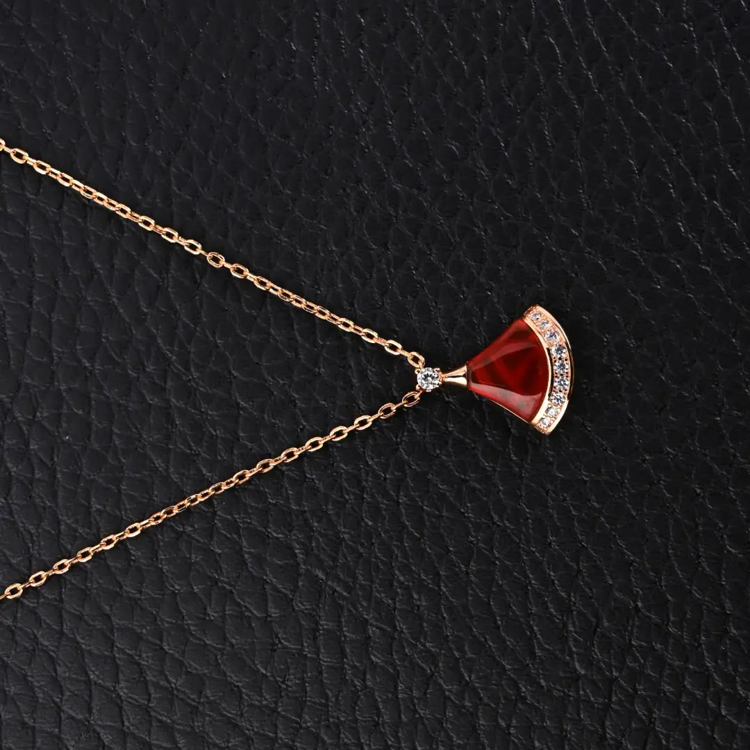BVLGARI Diva fan-shaped necklace featuring red agate and white mother of pearl, adorned with diamonds, displayed on a textured black background.