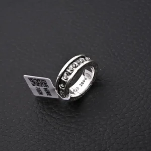 Chrome Hearts CH Cross Ring in vintage silver with decorative stones, showcasing price tag, placed on a dark textured surface.