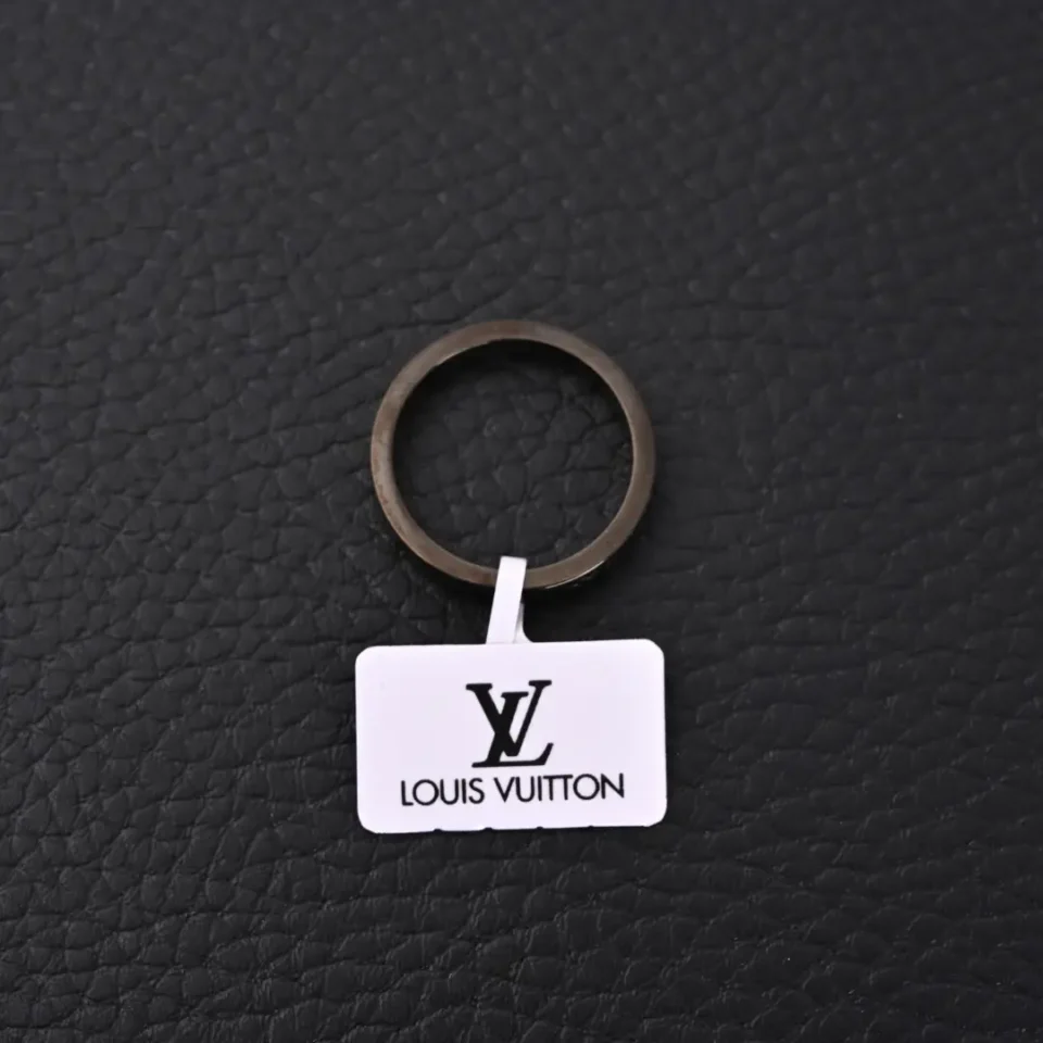 Louis Vuitton keychain white metal tag black logo accessory with round metal ring on black leather background