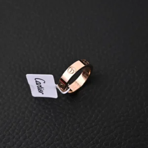 Cartier LOVE Series Ring in rose gold with tag, displayed on a textured black surface, highlighting luxury jewelry details.