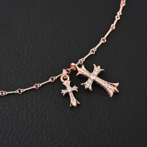 Chrome Hearts double cross pendant necklace featuring two intricately designed cross charms in rose gold, adorned with sparkling accents, displayed on a dark background.