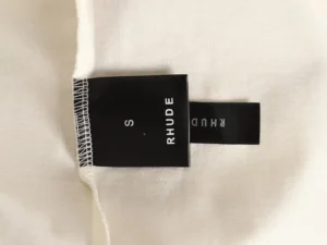 RHUDE clothing label displaying size 'S' on a white fabric background, relevant to the RHUDE 25ss retro logo print T-shirt product listing.