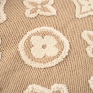 Louis Vuitton 3D embossed logo design on wool scarf, featuring intricate floral patterns in cream against a beige background, highlighting luxury fashion accessory details.