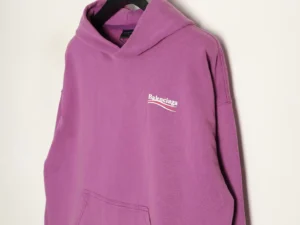Balenciaga Classic Cola Seal purple hoodie featuring logo detail, displayed on a hanger against a neutral background, emphasizing its stylish design for fashion enthusiasts.