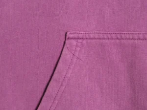 Close-up of a purple hoodie fabric featuring a pocket and visible stitching, representing the Balenciaga Classic Cola Seal hoodie.