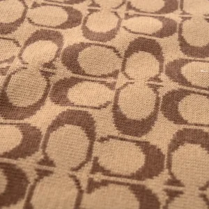 Coach Disney Double-Sided Logo Wool Scarf fabric featuring a repeating brown logo pattern on a beige background.