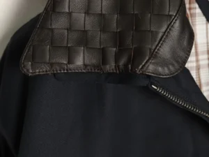 Bottega Veneta bag dark brown woven leather flap detail visible on black fabric background with zipper
