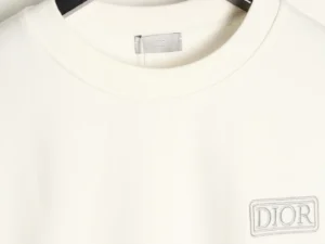 Close-up of a DIOR letter embroidered round neck sweatshirt, showcasing the brand logo on a cream-colored fabric.