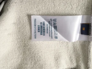 Label tag on a Louis Vuitton hoodie, displaying care instructions and fabric details, emphasizing quality craftsmanship and material composition.