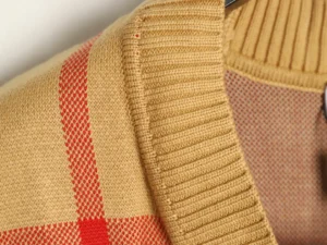 No brand or product type visible; image shows close-up of beige knit fabric with red woven pattern and ribbed texture.