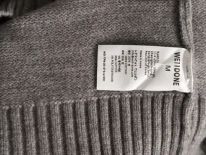 WE11 DONE gray sweater label showing size M and care instructions, emphasizing luxury fabric quality and minimalist design.