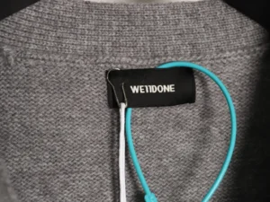 WE11 DONE label on a gray knit jacket with a turquoise drawstring, showcasing the brand's minimalist design and quality fabric.