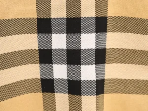 Burberry plaid patchwork stripes design featuring black, white, and beige colors, highlighting the textured fabric of the knitted sweater.