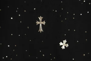 Chrome Hearts cross pin silver metal on black fabric background with scattered small studs accessory
