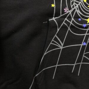 Close-up of SP5DER P*NK V2 Hoodie in black featuring a spider web design with colorful stars, showcasing premium fabric texture and unique graphic elements.