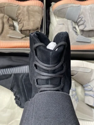 Yeezy Boost 750 black colorway suede sneakers with gum sole and velcro strap closure surrounded by other colorway pairs